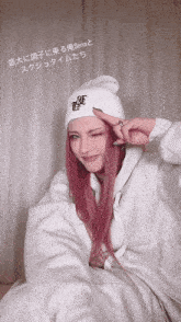 a woman with pink hair wears a white beanie with the letter e on it