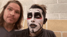 two men are standing next to each other and one has his face painted white and black