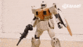 a toy robot is standing on a wooden floor holding a gun and shield .
