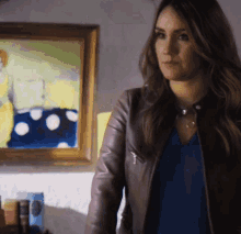 a woman in a leather jacket is standing in front of a framed painting
