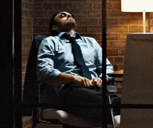 a man in a blue shirt and tie is sleeping in a chair