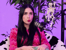 a woman in a pink sweater is sitting in front of a microphone with a skeleton in the background