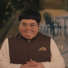 a man wearing glasses and a brown vest smiles