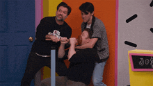 a man wearing a black shirt that says no goodies is being held by two other men