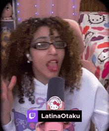 a woman wearing glasses and a hello kitty sweatshirt is holding a microphone and says latinaotaku