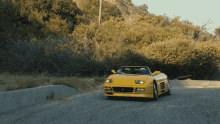 a yellow car is driving down a road with trees in the background