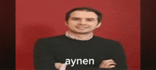a man in a black sweater and tie is standing in front of a red background .