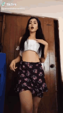 a woman wearing a crop top and a floral skirt is standing in front of a wooden door ..