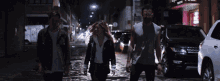 a group of people walking down a street at night with a sign that says ' barber shop ' on it