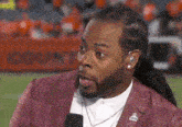 a man with dreadlocks is talking into a microphone on a football field .