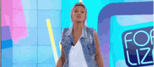 a woman wearing a denim vest is standing in front of a sign that says for liz