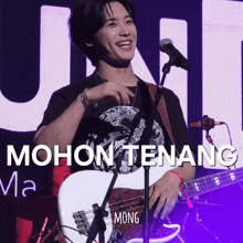 a man singing into a microphone while holding a guitar with the words mohon tenang on the bottom