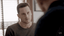 a man in a sweater is talking to another man in front of a window .