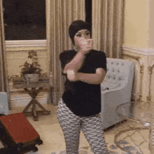 a woman in a black shirt and zebra print pants is standing in a living room with her arms crossed .