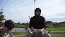 a man wearing a black hoodie sits on a bull