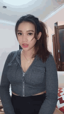 a woman wearing a gray crop top and a necklace with the letter i on it