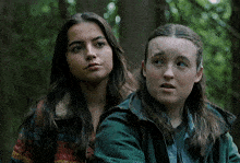 two girls are standing next to each other in the woods and one is wearing a green jacket