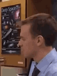 a man in a blue shirt and tie is sitting in front of a poster on a wall that says deep space .