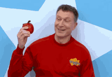 a man wearing a red sweater with the wiggles logo on it holds an apple