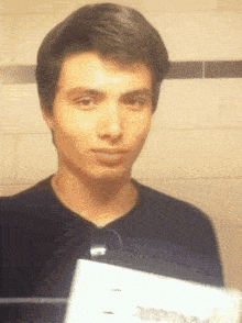 a man in a black shirt is holding a piece of paper in front of his face