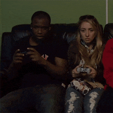 a man wearing a true religion shirt sits next to a woman holding a video game controller