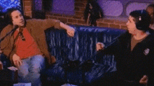 a man and a woman are sitting on a blue couch talking into microphones .