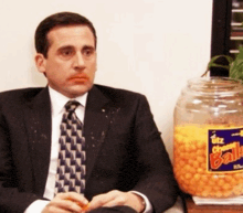a man in a suit and tie sits in front of a jar of totz cheese balls