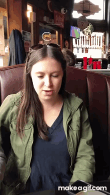 a woman in a green jacket sits in a booth at a restaurant with a sign that says potfest in the background