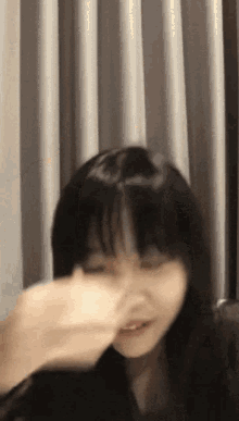 a woman with long black hair is blowing her nose in front of a curtain .