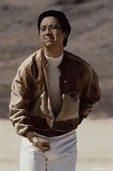 a man wearing glasses and a brown jacket is standing on a beach .