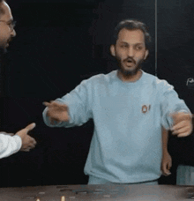 a man with a beard is standing in front of a table talking to another man .