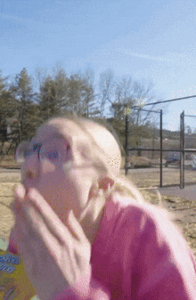 a woman wearing glasses and a pink shirt is eating a box of chex mix