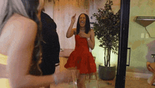a woman in a red dress is laughing while standing next to a plant