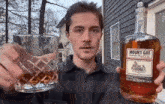 a man is holding a glass and a bottle of mount gay black barrel