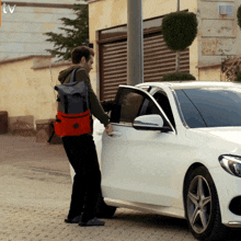 a man with a backpack is getting into a white car with the tv logo on the bottom