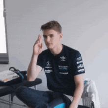 a young man wearing a mercedes shirt is sitting on a bench with his hand on his forehead .