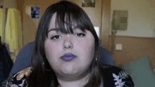 a woman with purple lipstick is sitting in a chair and making a funny face .