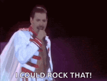 a man in a white coat is singing into a microphone and saying `` i could rock that ! ''