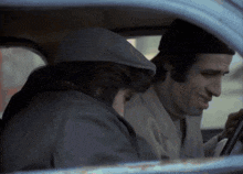 two men are sitting in a car one wearing a hat