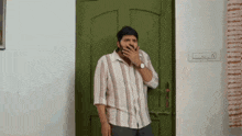 a man in a striped shirt is covering his mouth in front of a green door