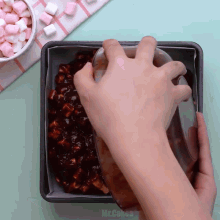 a person pouring chocolate sauce into a pan with marshmallows on the table