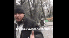 a man wearing a black hat and a black coat is standing in a park with the words la televiziar asmarati written below him