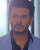 a man with a beard is wearing a light blue jacket and black shirt