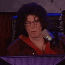 a man with curly hair and glasses is sitting in front of a microphone in front of a computer monitor .