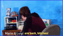 a man sits at a desk with the words " mario & luigi are back bitches " above him