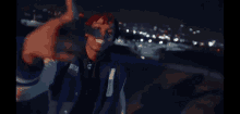 a man with red hair is standing on top of a building at night and pointing at the camera .