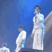 a man is standing on a stage holding a microphone while another man stands behind him .