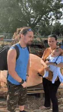 a man and woman are holding a baby in front of a large pumpkin .