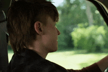 a young man driving a car looks out the window
