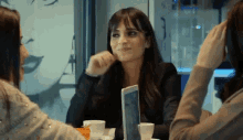 a woman is sitting at a table with two other women and a tablet